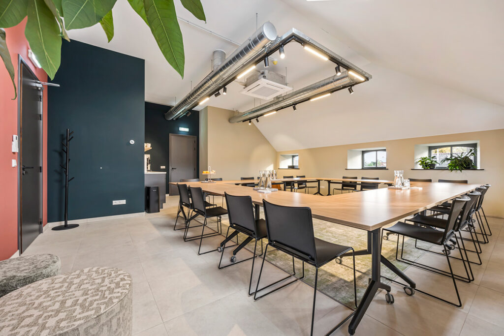 Een ruime en lichte vergaderruimte bij Onder de Pannen in Echt, ingericht met een U-vormige tafelopstelling, zwarte stoelen en een industriële plafondafwerking.