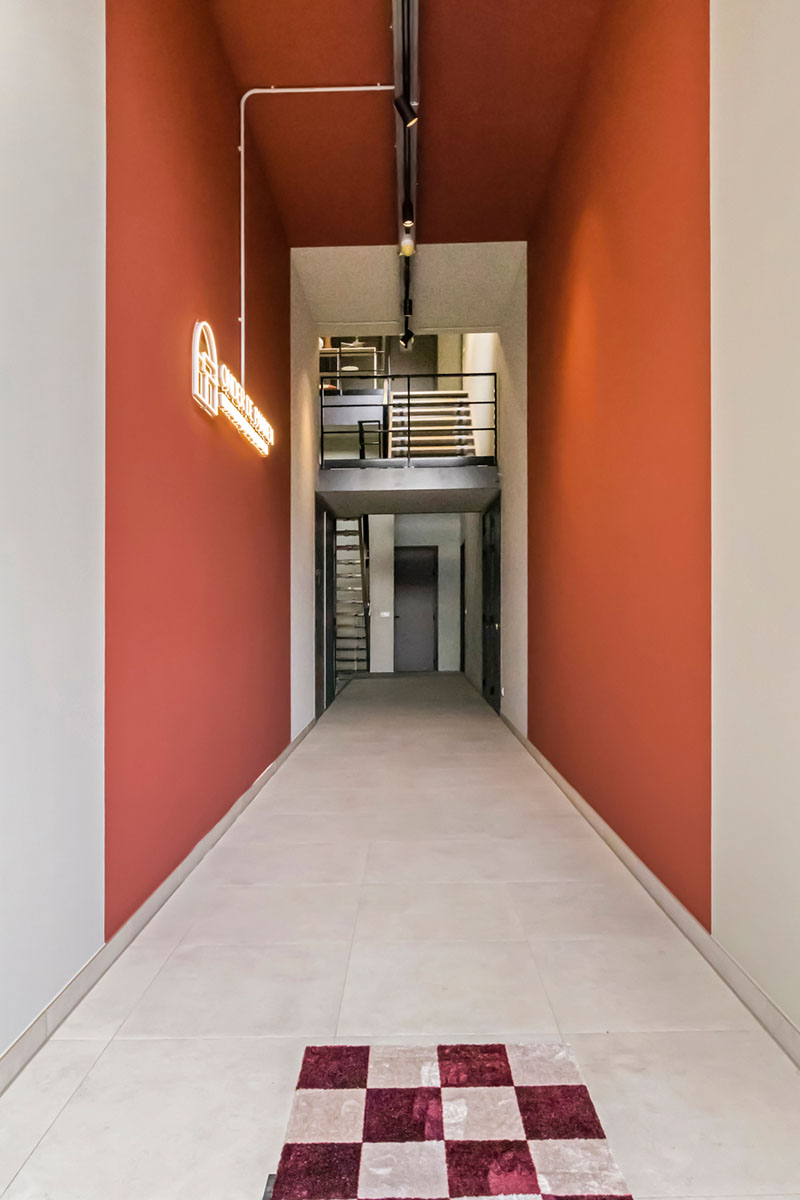 Sfeervolle entree van Onder de Pannen in Echt, met hoge rode muren, een moderne trap en een neonlogo aan de muur.