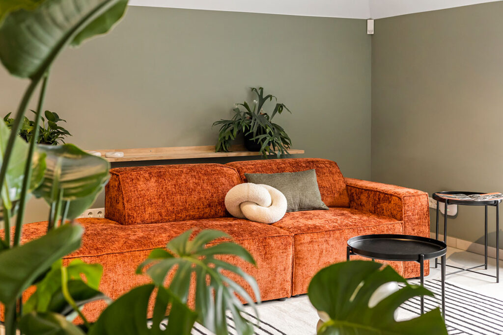 Sfeervolle loungehoek in Onder de Pannen, met een comfortabele roestkleurige bank, groene planten en een knusse sfeer voor ontspanning tijdens vergaderingen.