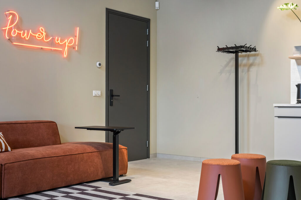 De binnenkant van de studio ruimte met een bank, tafeltje, neon bord en dichte deur